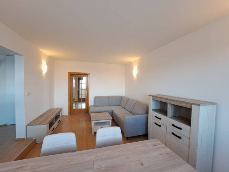 Obývací pokoj ve 4pokojovém bytě s podlahou s dřevěným dekorem a šedou sedačkou.