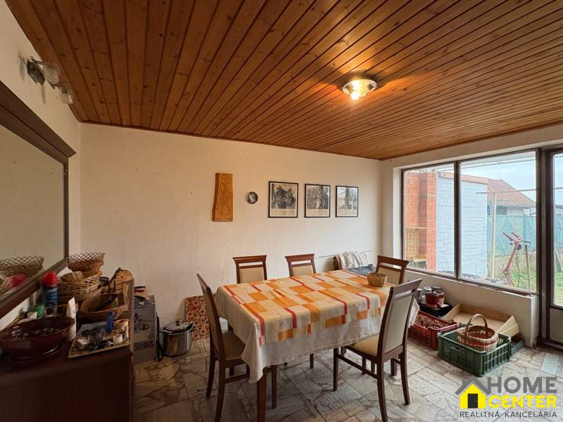 Jídelna v rodinném domě s dřevěným stropem, čtvercový stůl, velké okno.