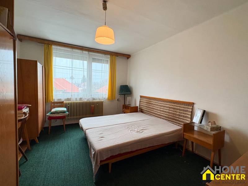 Ložnice s jednoduchým nábytkem v rodinném domě, zelený koberec a žluté záclony.