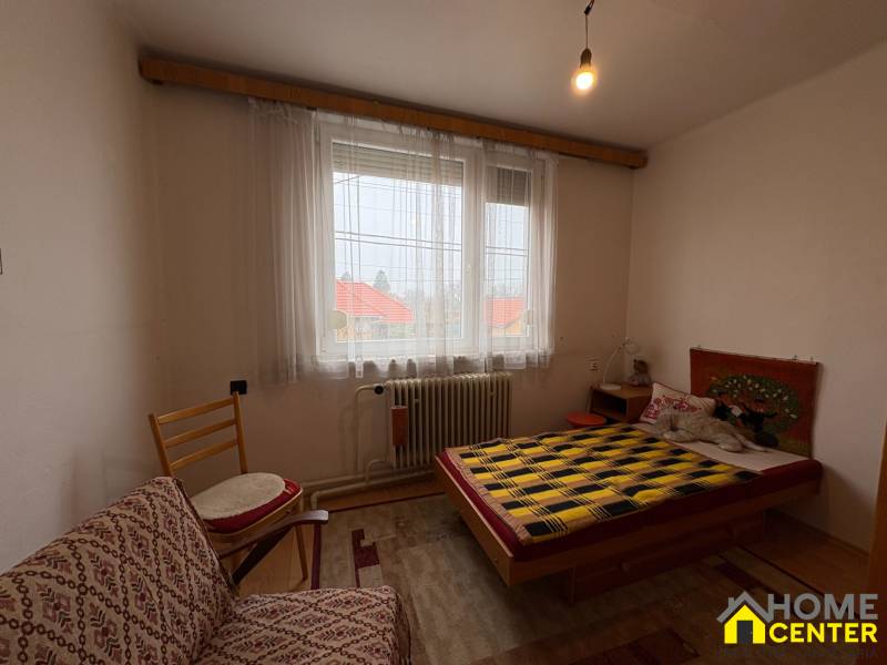 Pokoj s postelí, křeslem a dekorativním kobercem na stěně v rodinném domě.