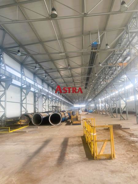 Výrobní prostory s kovovými konstrukcemi a potrubím, Dobšiná. Široká hala se žlutými zábranami.