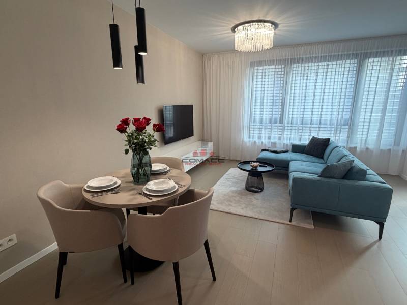 Obývací pokoj v dvoupokojovém bytě s šedou sedačkou, jídelním stolem a podlahou s dřevěným dekorem.