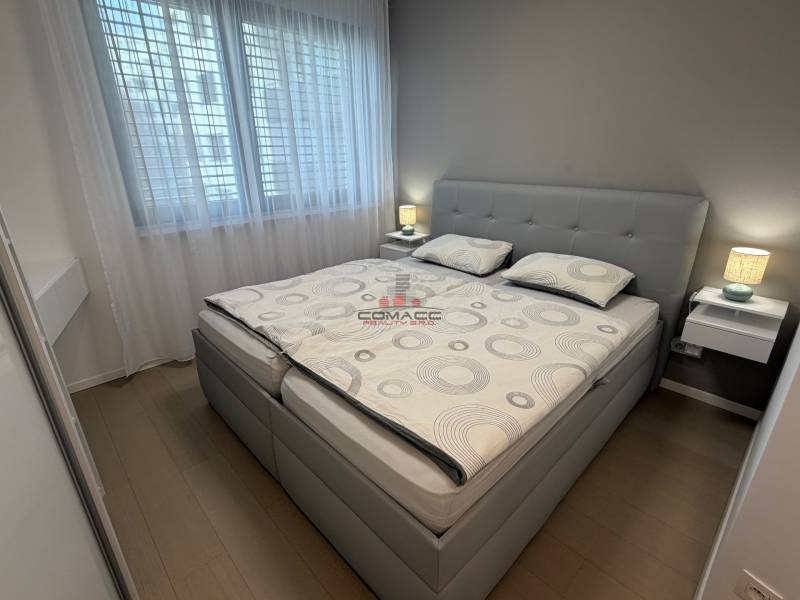 Ložnice v 2-pokojovém bytě s postelí, nočními stolky a podlahou s dřevěným dekorem.