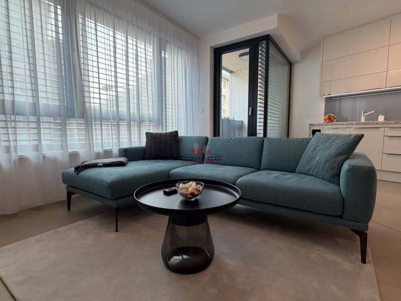 Obývací pokoj s pohovkou, stolkem a kuchyňským koutem v 2-pokojovém bytě.