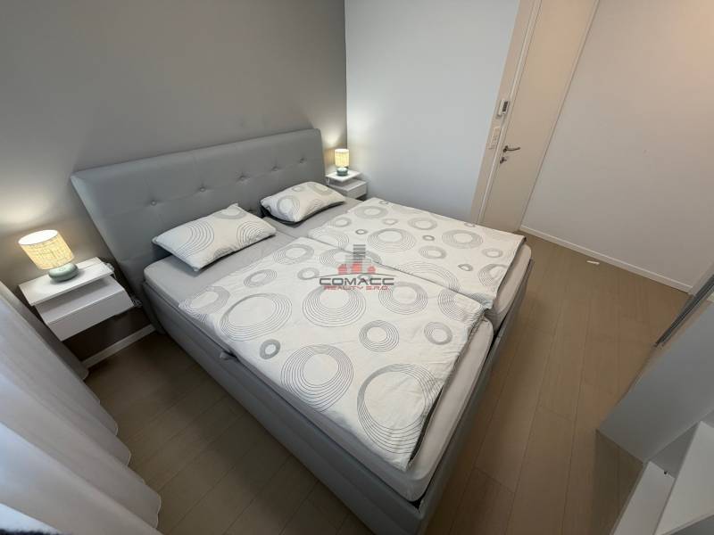 Ložnice s manželskou postelí a podlahou s dřevěným dekorem v dvoupokojovém bytě.