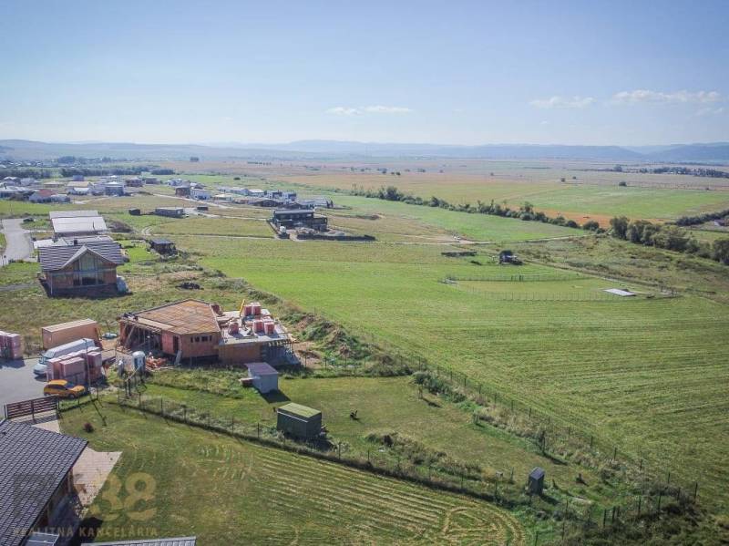 Pozemky - bydlení v Mlynici; rozestavěné domy a rozsáhlá pole pod slunečnou oblohou.