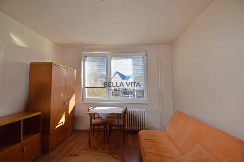 Garsonka s pohovkou, stolem a skříní, podlaha s dřevěným dekorem.