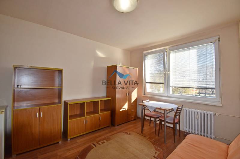 Garsonka s nábytkem, stolem a židlemi, doplněná podlahou s dřevěným dekorem.