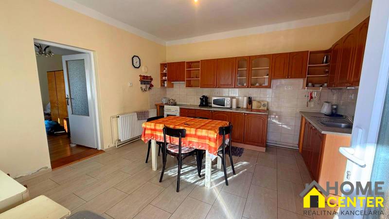 Kuchyně v rodinném domě s dřevěným dekorem a oranžovým ubrusem na stole.