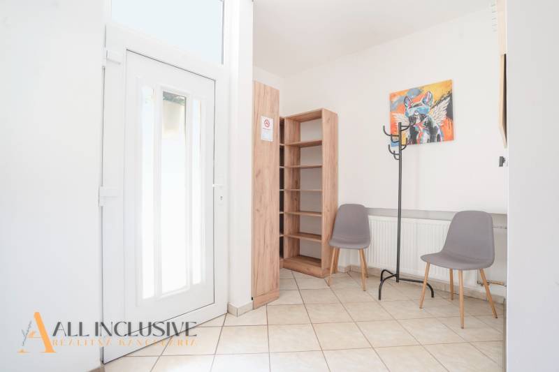 Interiér budovy se vstupními dveřmi, dlažbou, poličkou, dvěma židlemi a věšákem.