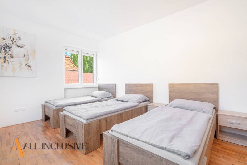 Tři postele v pokoji s podlahou s dřevěným dekorem a obrazem na stěně.