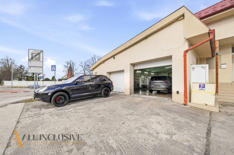 Budova v Dunajské Stredě s automobily před garážemi a dopravními značkami.