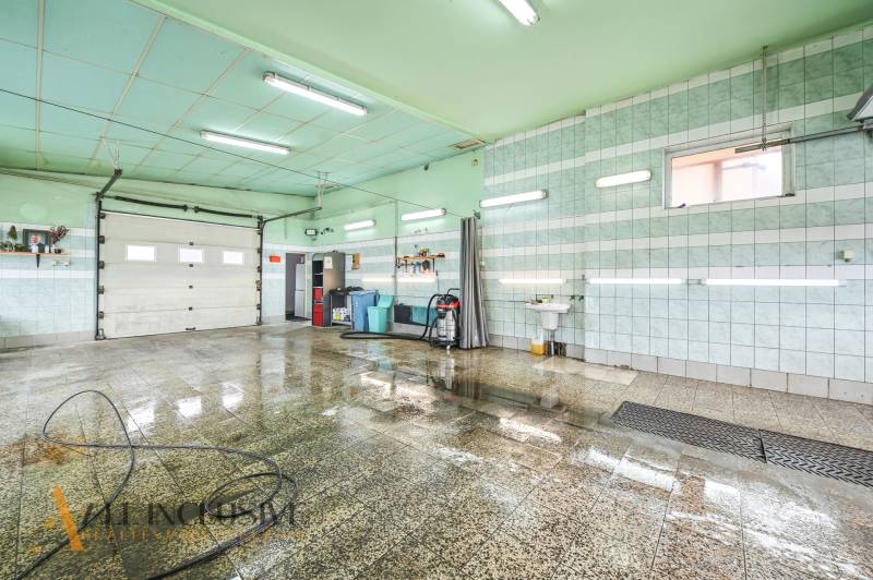 Místnost v budově s mokrou dlažbou, umyvadlem a hadicí na stěně.