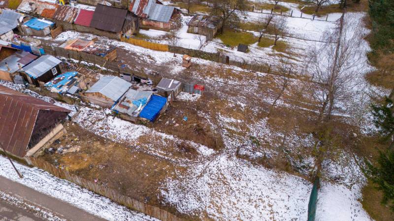 Zimní zahrada v Nálepkově se zasněženými chatkami a stromy, kontrastující s hnědou půdou.
