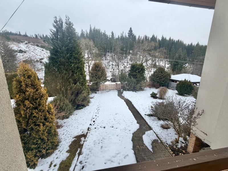 Zasněžená zahrada rodinného domu v Čadci na ulici Čadečka s jehličnany a trávníkem.