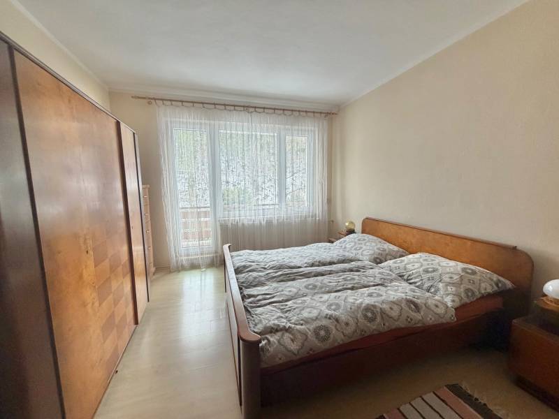 Ložnice s manželskou postelí, skříní a podlahou s dřevěným dekorem v rodinném domě.