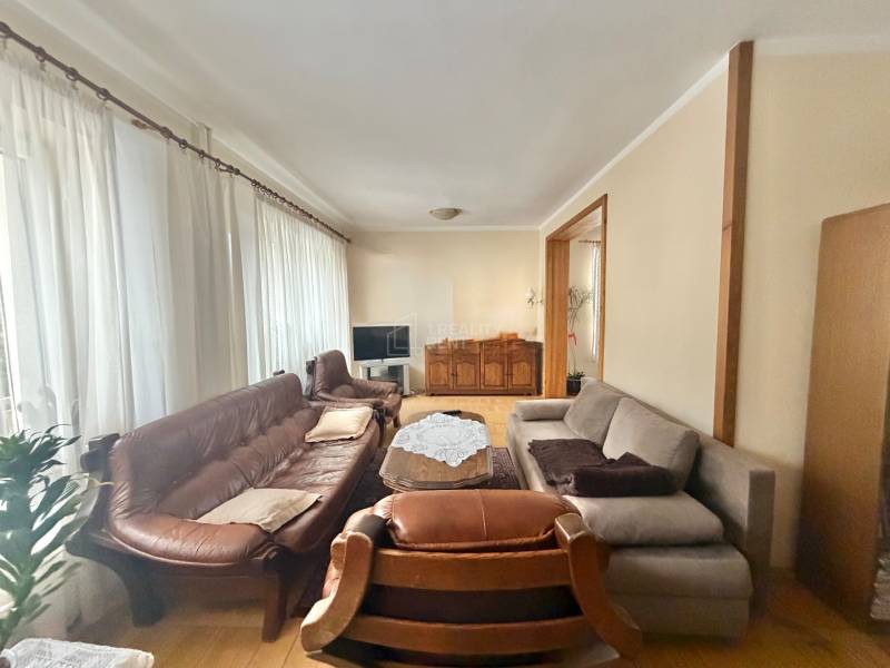 Obývací pokoj v rodinném domě s podlahou s dřevěným dekorem, sedačkou a záclonami.