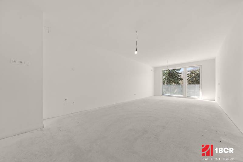 Prostorná místnost ve 4pokojovém bytě s velkým francouzským oknem a bílými stěnami.