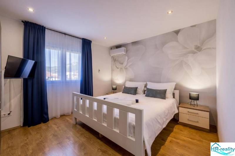 Světlá ložnice s TV, klimatizací a podlahou s dřevěným dekorem ve vile.