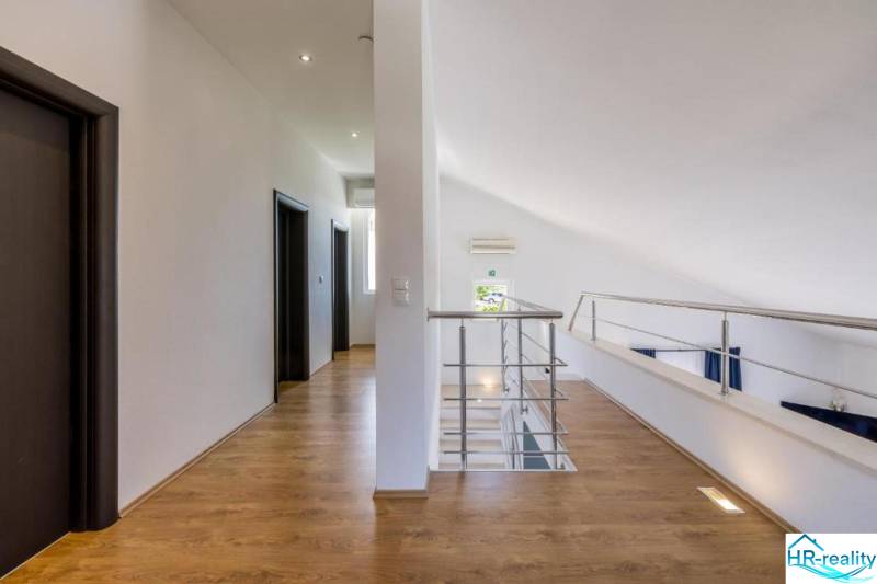 Interiér vily s bílými stěnami, podlahou s dřevěným dekorem a zábradlím.