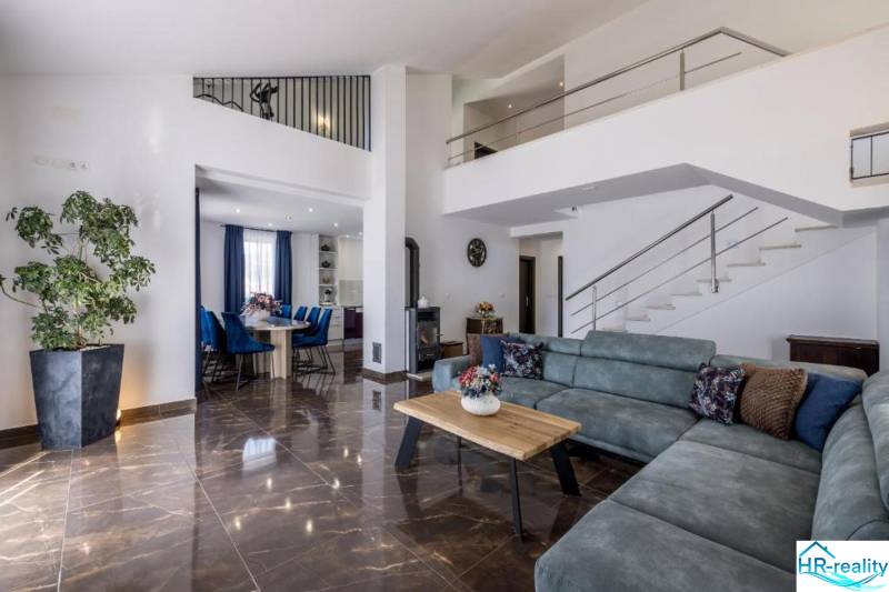 Obývací pokoj vily s pohodlnou sedačkou, jídelnou a schodištěm, podlaha s dřevěným dekorem.