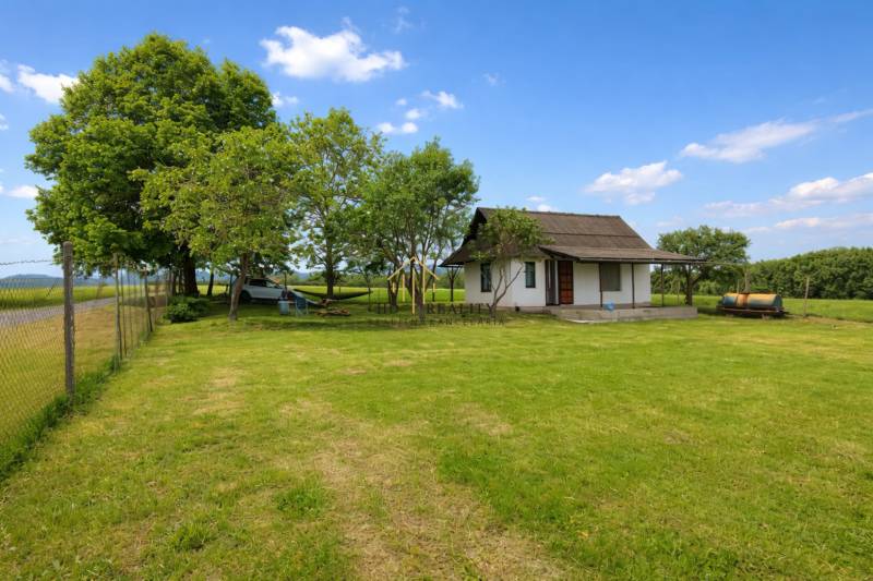 Chata v Obeckově obklopená přírodou s udržovaným trávníkem a dřevinami.