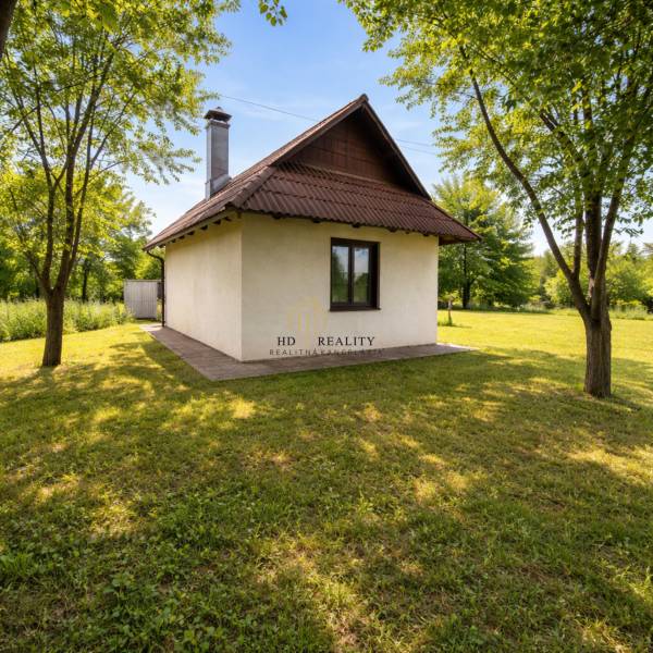 Chata v Obeckově obklopená zeleným trávníkem a stromy.