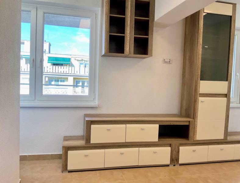 Obývací stěna v 1-pokojovém bytě s podlahou s dřevěným dekorem a výhledem z okna.