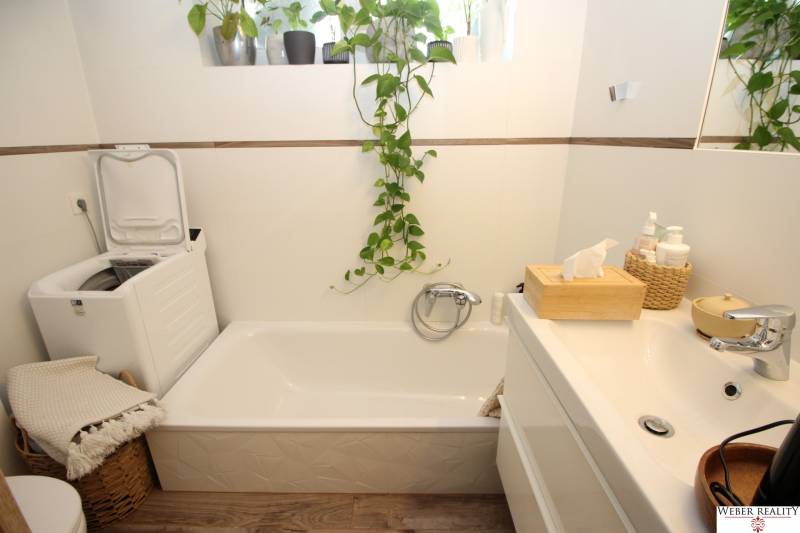 Koupelna v 1-pokojovém bytě s vanou, pračkou a dřevěným dekorem na podlaze.