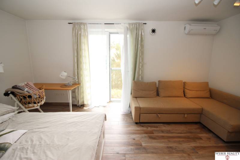 1-pokojový byt s gaučem, postelí, psacím stolem a podlahou s dřevěným dekorem.