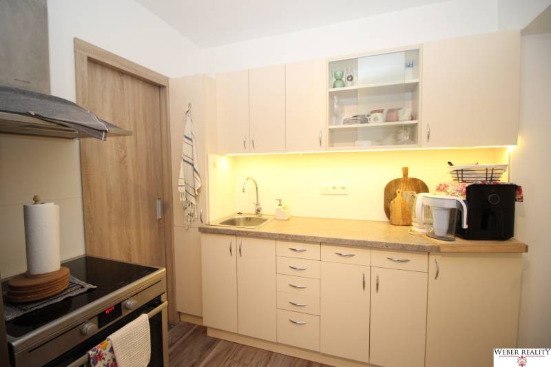 Kuchyně v 1-pokojovém bytě se světlým nábytkem a podlahou s dřevěným dekorem.