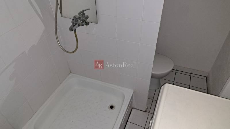 Koupelna v 1-pokojovém bytě s bílým obkladem a sprchovým koutem.