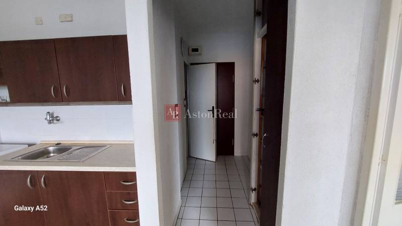 Kuchyně s tmavými skříňkami a bílými obklady v 1-pokojovém bytě.