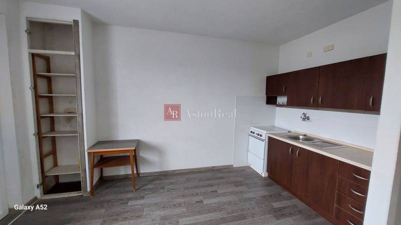 Kuchyně v 1-pokojovém bytě s tmavými skříňkami a podlahou s dřevěným dekorem.