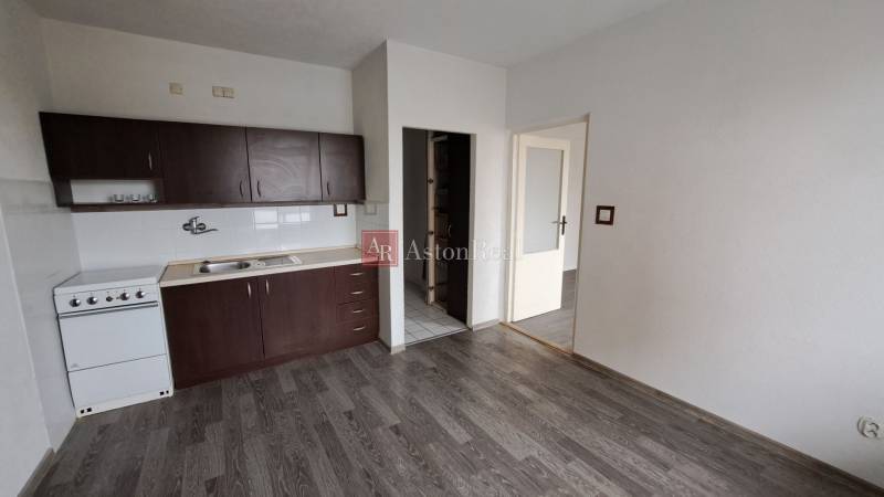 Kuchyně s tmavými skříňkami a podlahou s dřevěným dekorem v 1-pokojovém bytě.