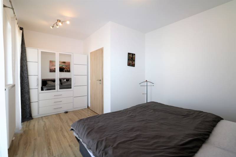 Ložnice v 2-pokojovém bytě s podlahou s dřevěným dekorem, šatníkem a postelí.