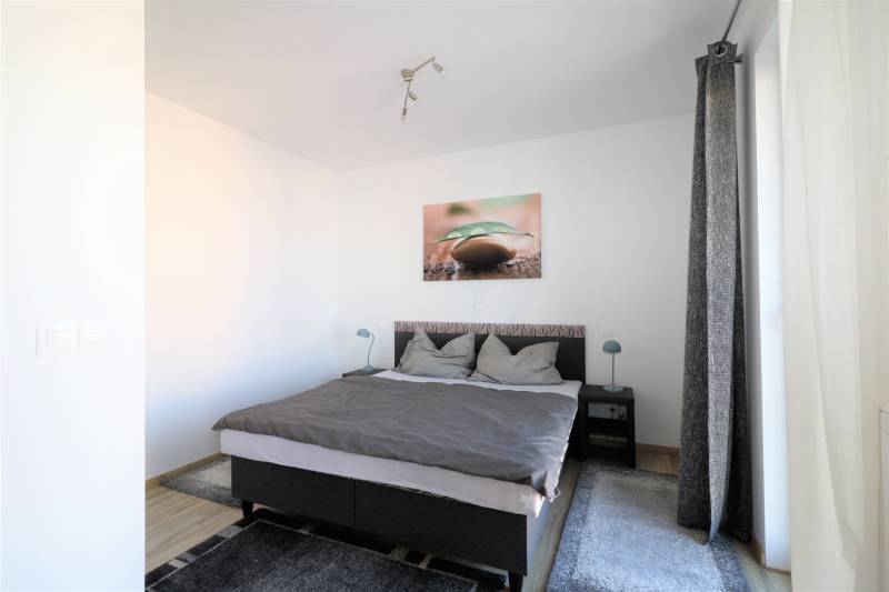 Světlá ložnice v 2pokojovém bytě s pohodlnou postelí a kobercem.