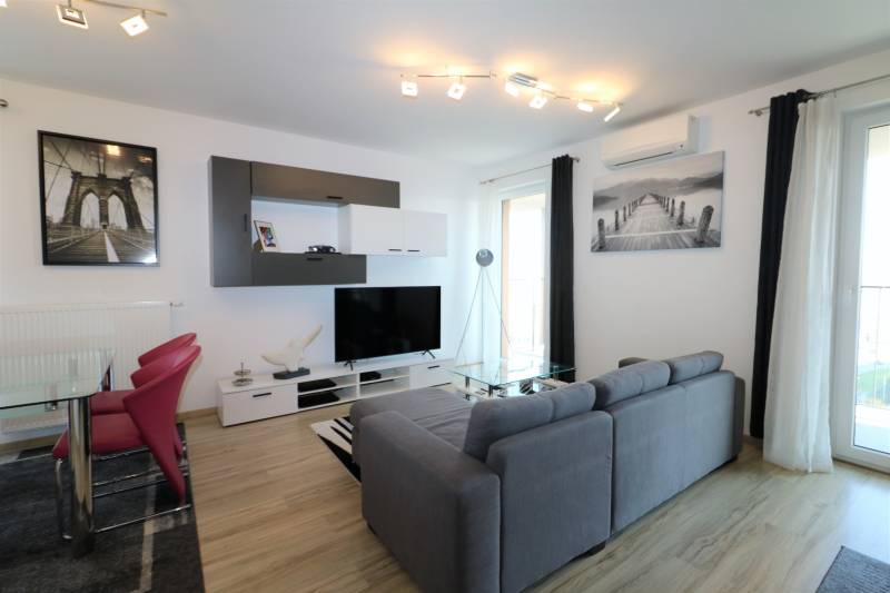 Obývací pokoj v 2-pokojovém bytě s pohovkou, TV, podlahou s dřevěným dekorem.