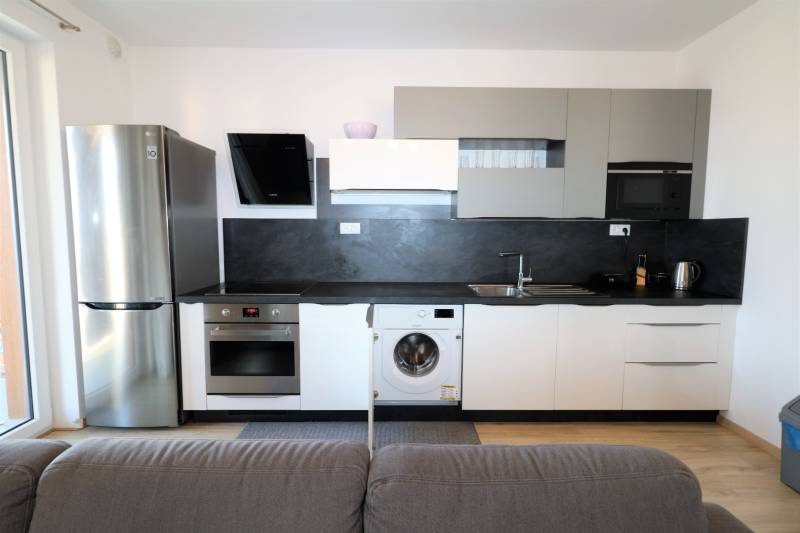 Kuchyně v 2-pokojovém bytě se šedými skříňkami, spotřebiči a podlahou s dřevěným dekorem.