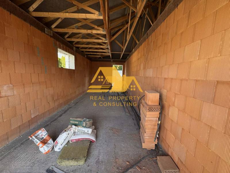 Stavba rodinného domu na ulici v Nových Zámcích s cihlovými stěnami a trámovým stropem.