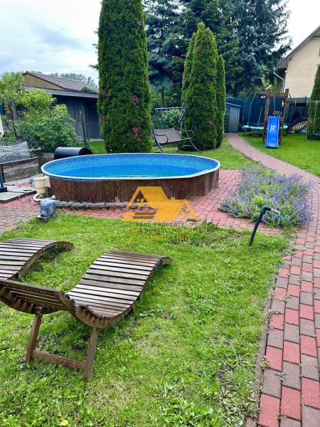 Zahrada chaty v Nových Zámcích s bazénem, lehátky a dětským hřištěm.