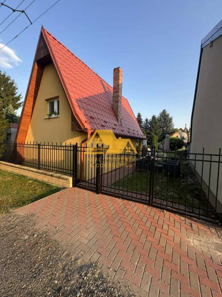 Chata na ulici v Nových Zámcích, se špičatou střechou a cihlovým komínem.