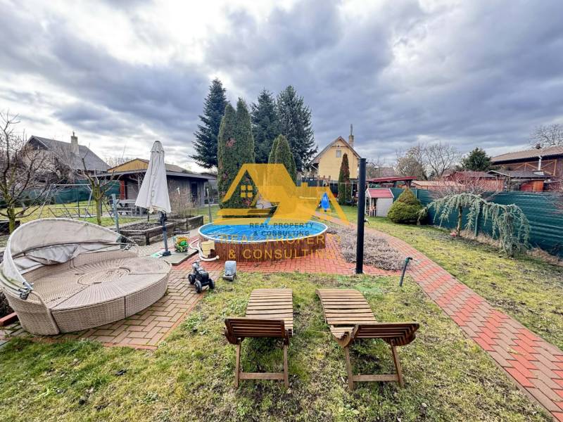 Zahrada u chaty s bazénem na ulici v Nových Zámcích, obklopená udržovanou zelení.