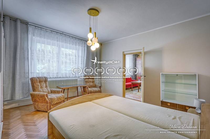 Ložnice rodinného domu se světlým dřevěným nábytkem a pohodlnými křesly.