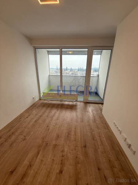 Obývací pokoj v 1-pokojovém bytě s podlahou s dřevěným dekorem a velkými okny.