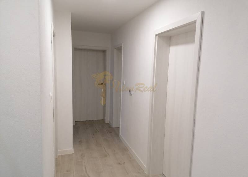 Úzká chodba v rodinném domě s bílými stěnami a podlahou s dřevěným dekorem.