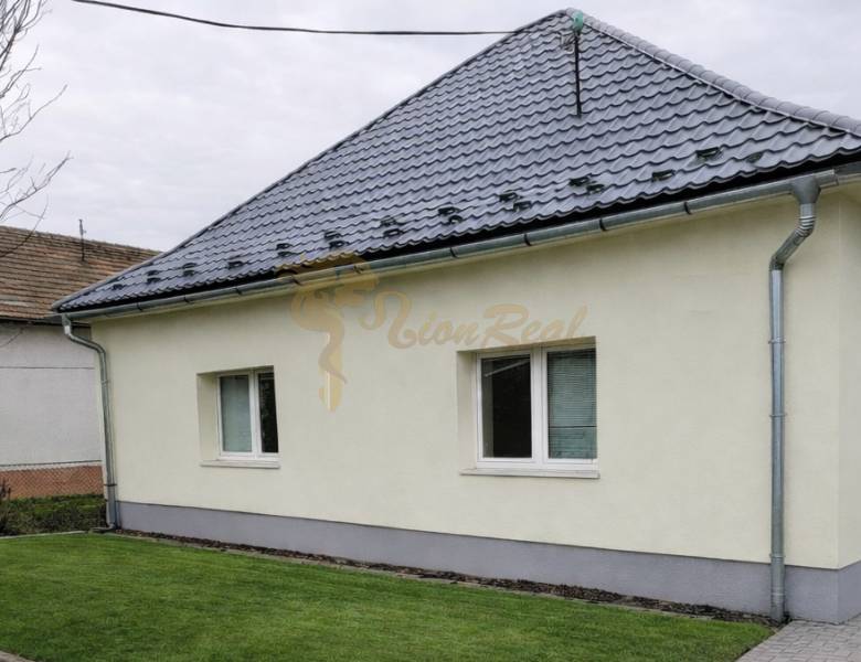 Rodinný dům v Bernolákově s trávníkem, šedou střechou a světlou fasádou.