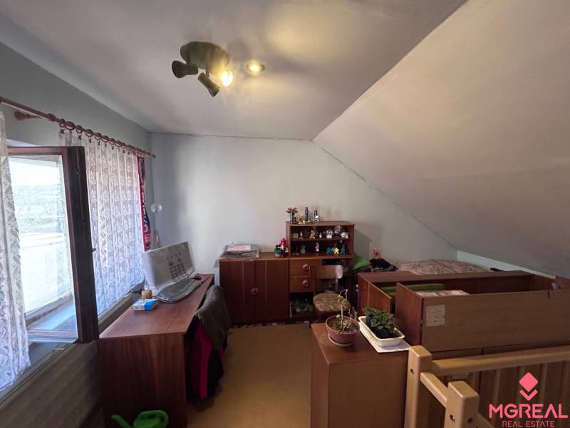 Podkrovní pokoj s pracovním stolem a postelí v rodinném domě.