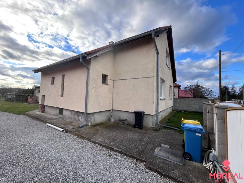 Rodinný dům v Zbechách s vedlejší cestou, trávníkem a modrou popelnicí.