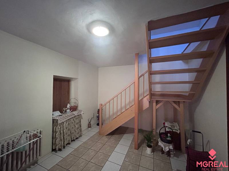 Interiér rodinného domu s dřevěným schodištěm, stolkem a podlahou z keramických dlaždic.